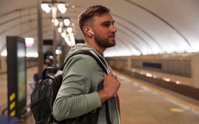 Photo of young adult man wearing earbuds waiting for public transit.