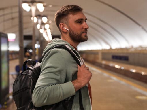 Photo of young adult man wearing earbuds waiting for public transit.