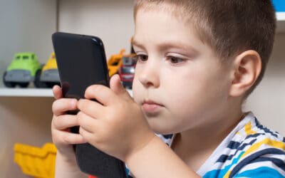 A young child looks at a mobile phone screen that he is holding very close to his face.
