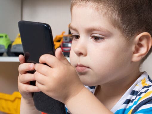 A young child looks at a mobile phone screen that he is holding very close to his face.