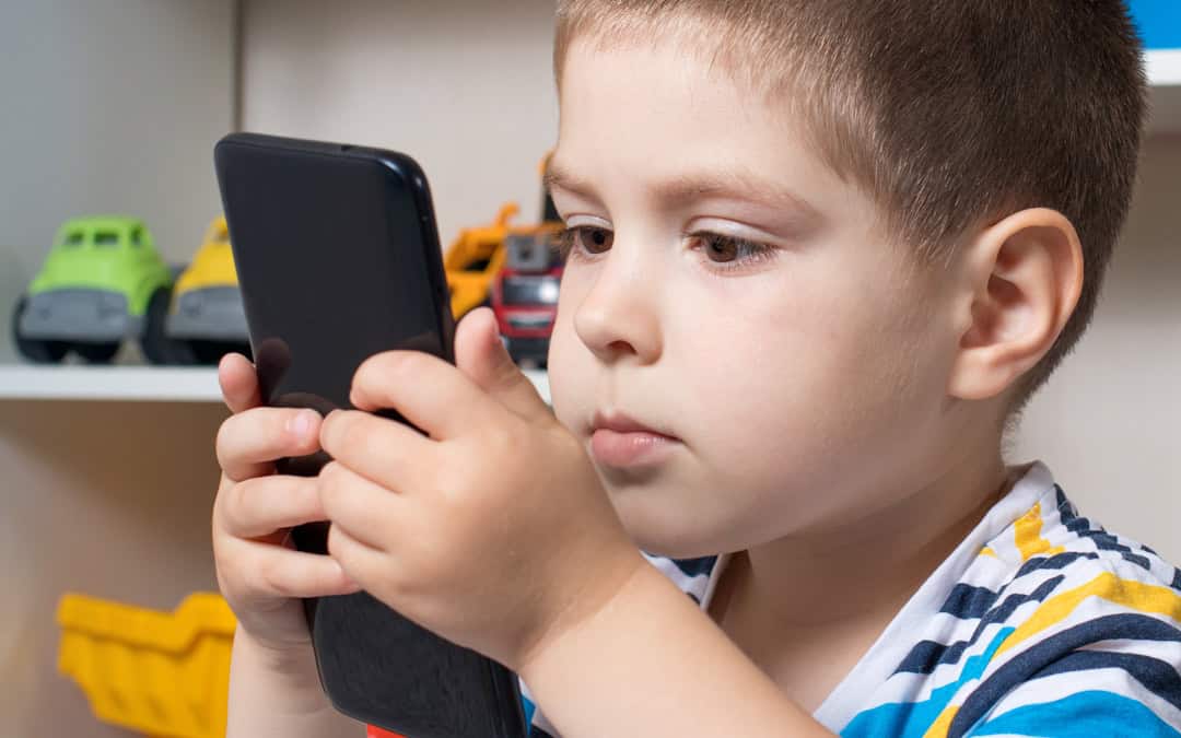 A young child looks at a mobile phone screen that he is holding very close to his face.