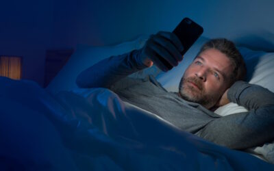 man at night in bed looking at cell phone with exposure to blue light