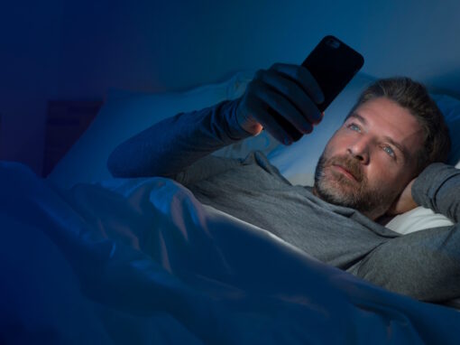 man at night in bed looking at cell phone with exposure to blue light